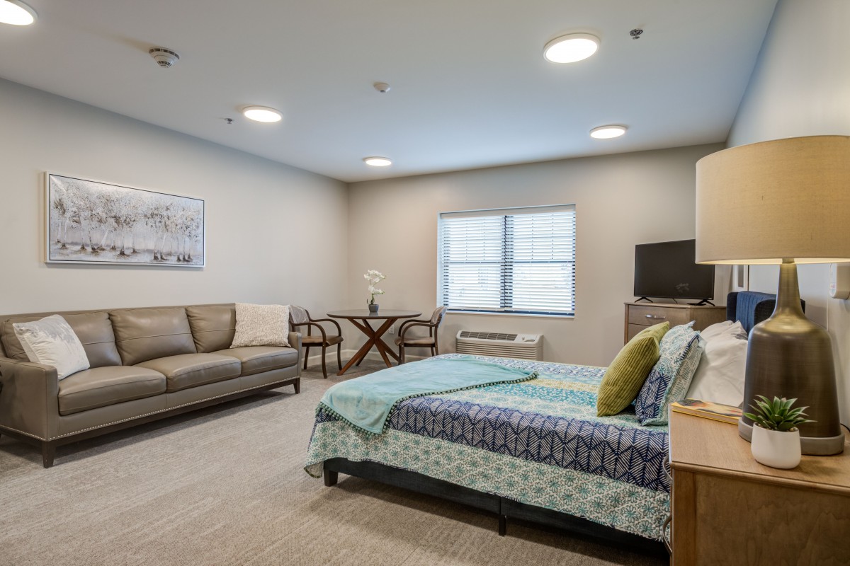 A spacious bedroom with a sofa, bed, and dining area in a well-lit interior setting.