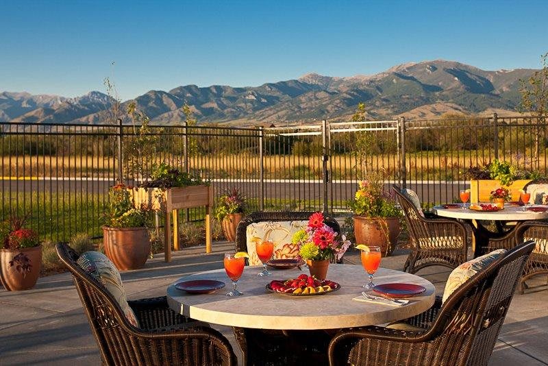 A picturesque outdoor dining setup with a mountain view, featuring a table with drinks and floral centerpiece.