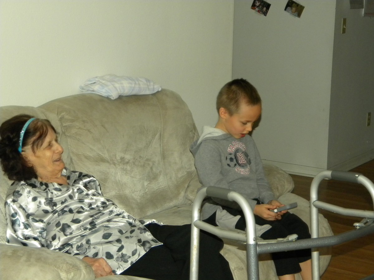 A child sits quietly beside an elderly person resting on a sofa in a living room.
