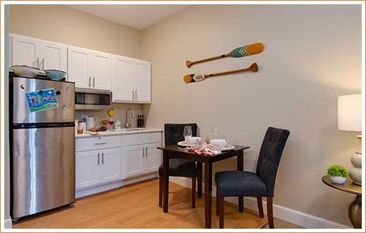 A cozy kitchen and dining area with modern appliances, a small table set for two, and decorative paddles on the wall.