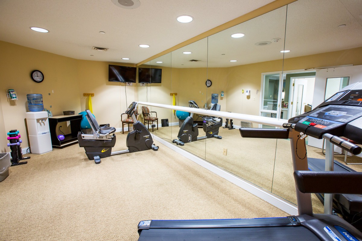 A well-equipped gym room with a treadmill, stationary bikes, and large mirrors.