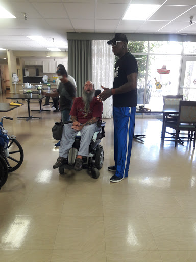 A caregiver provides assistance to an elderly individual in a wheelchair in a rehabilitation facility.