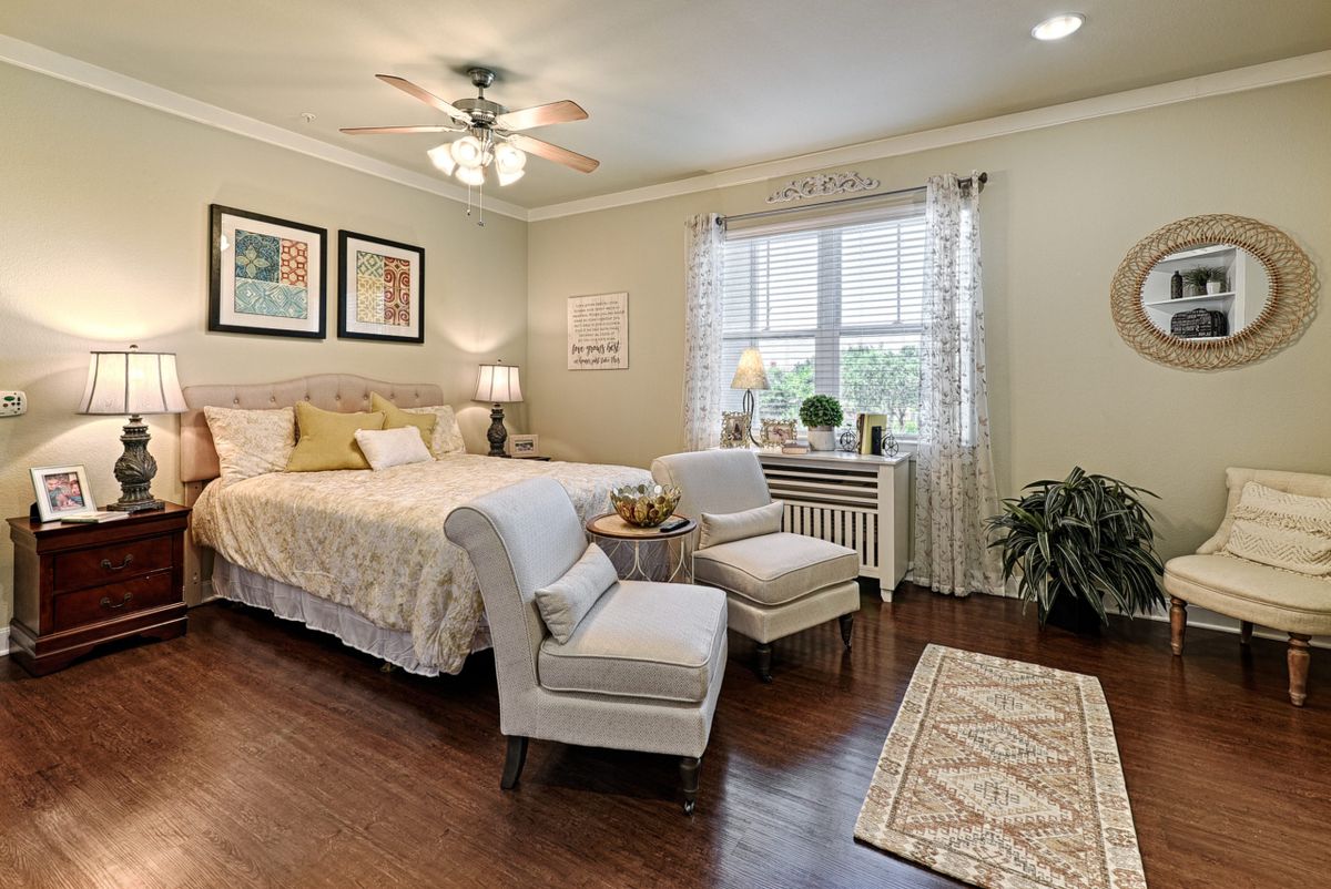 A cozy and elegantly designed bedroom featuring a comfortable bed, two chairs, and tasteful decorations with natural light streaming through the window.