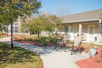 A serene garden setting with a pathway, benches, and surrounding trees near a building.