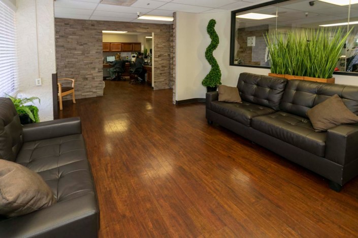 A modern office waiting area with black leather sofas and green plants.