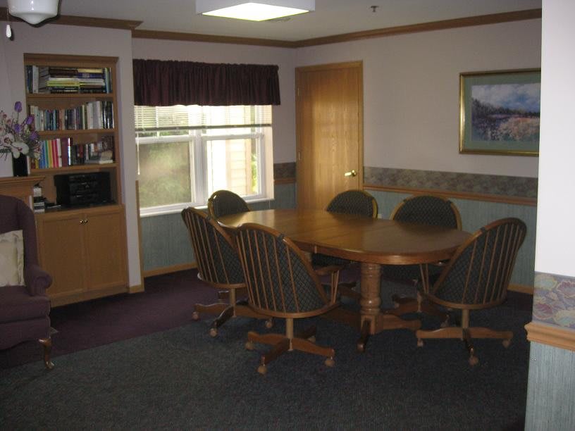 A small conference room with a round table and chairs, featuring a window and bookshelf.