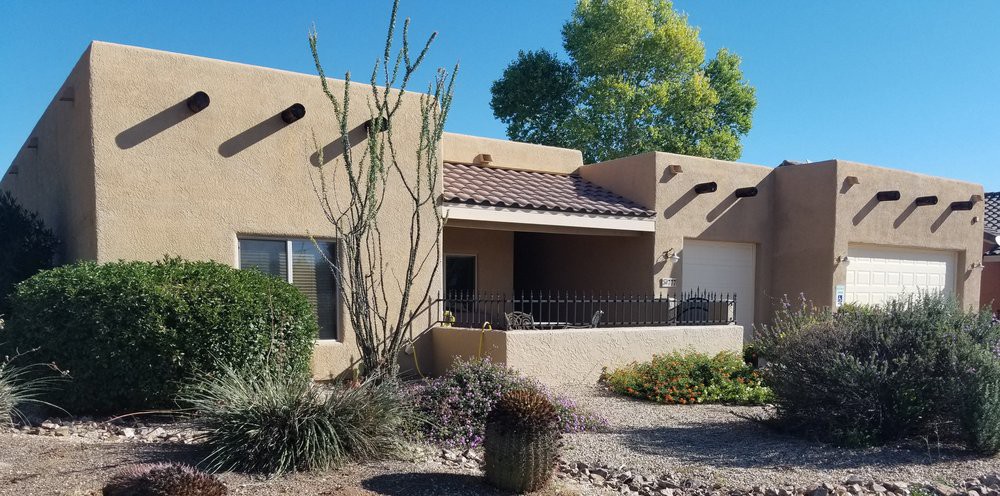 A southwestern-style stucco house with desert landscaping, featuring cactus plants and a cozy outdoor patio on a sunny day.