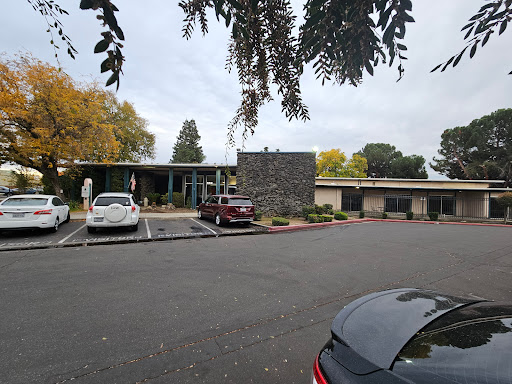 A view of a modern building with an adjoining parking lot, surrounded by autumn foliage.