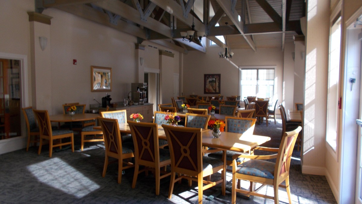 An empty dining area with wooden tables and chairs illuminated by sunlight.