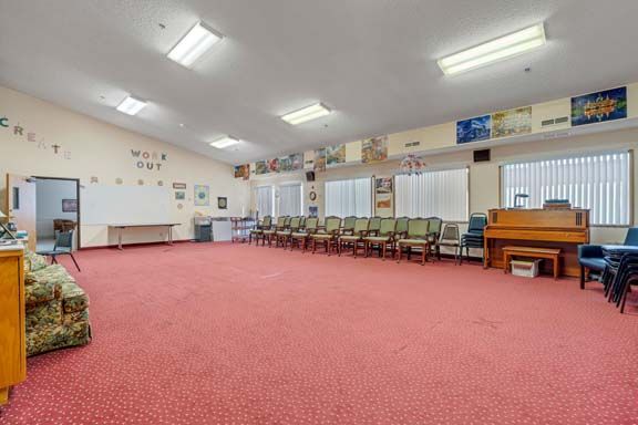 An empty classroom with a row of chairs, a piano, and colorful decorations on the walls.