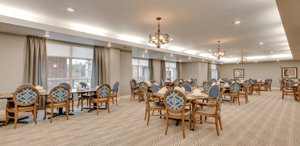 An elegantly decorated dining area with wooden tables and chairs, soft lighting from chandeliers, and large windows.