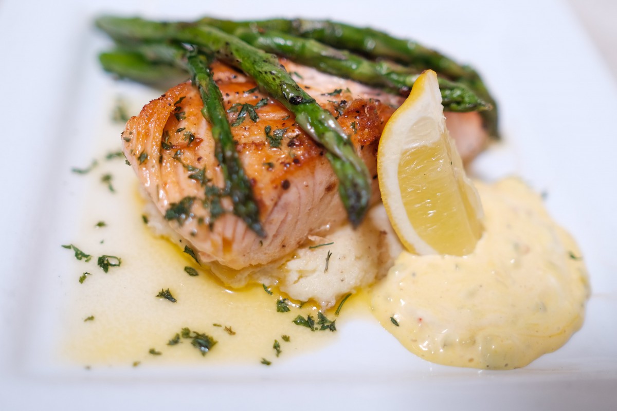 Grilled salmon served with asparagus, lemon, and creamy sauce.