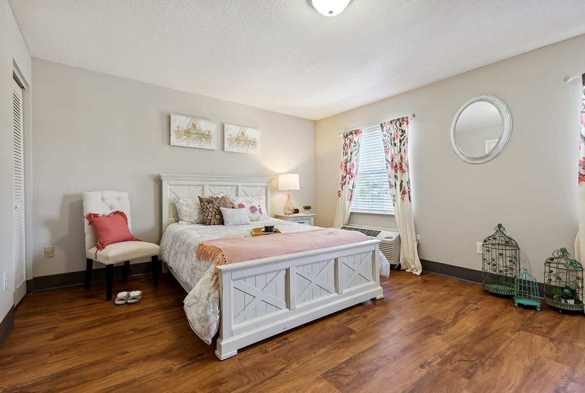 A cozy bedroom featuring a large bed with decorative pillows, a wooden floor, and natural light streaming in through a window.