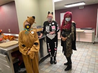 Three people dressed in Halloween costumes and masks, standing indoors.