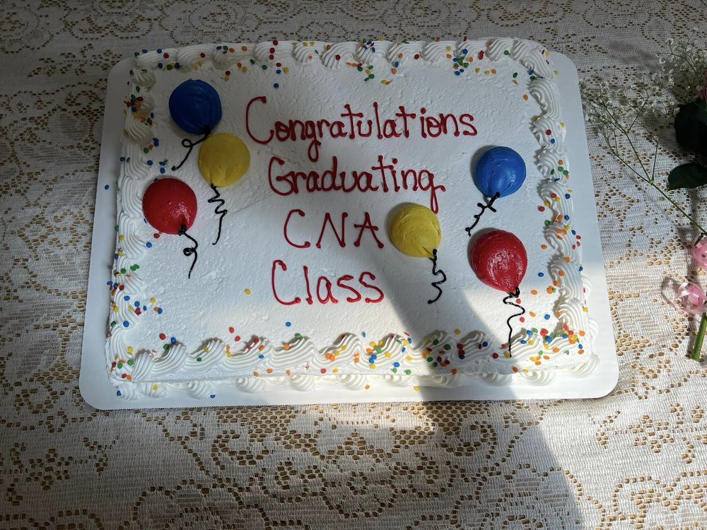 A celebratory cake for a graduating CNA class, decorated with colorful balloons and congratulatory text.