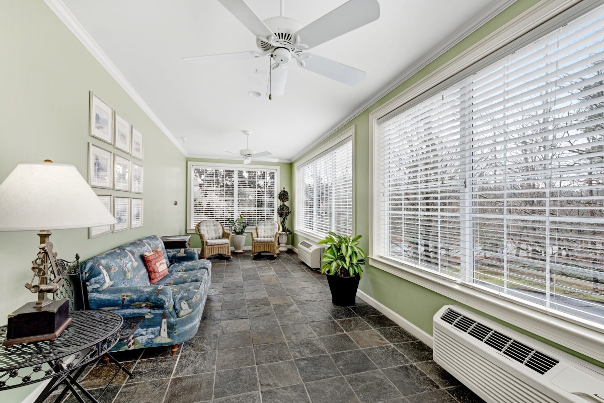A bright sunroom featuring large windows, comfortable seating, and decorative plants.