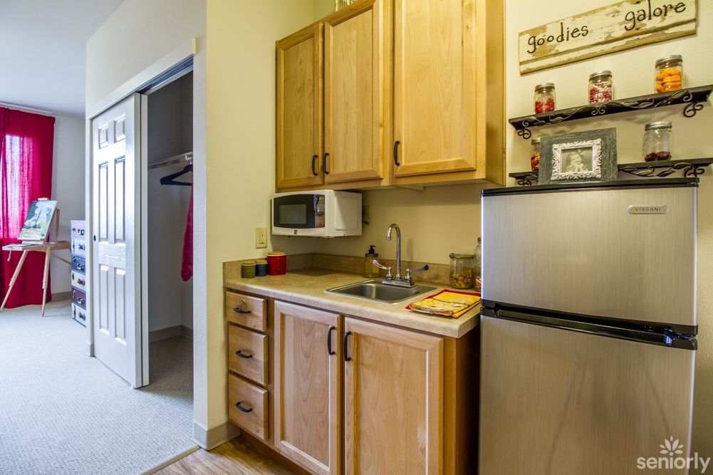 A compact kitchen area featuring wooden cabinets, a microwave, a small refrigerator, and a sink.