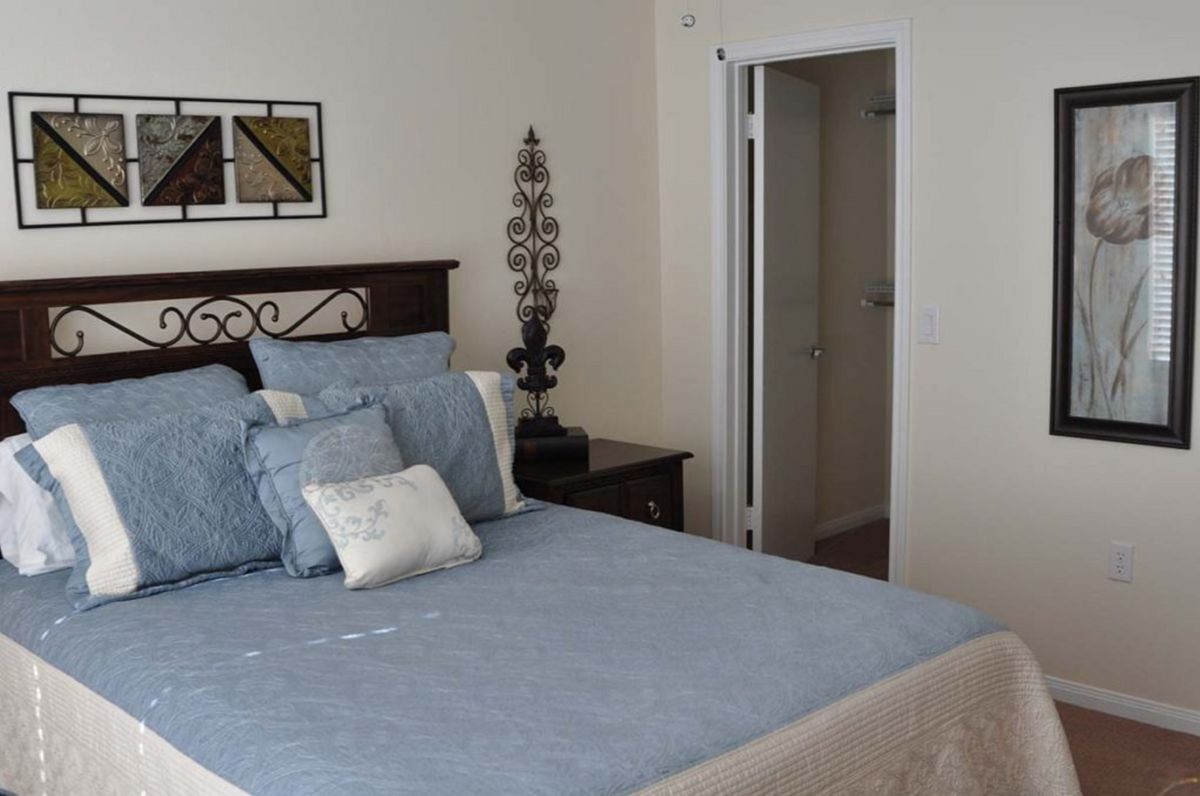 A cozy bedroom with light blue bedding and decorative pillows, featuring a nightstand and an open doorway.