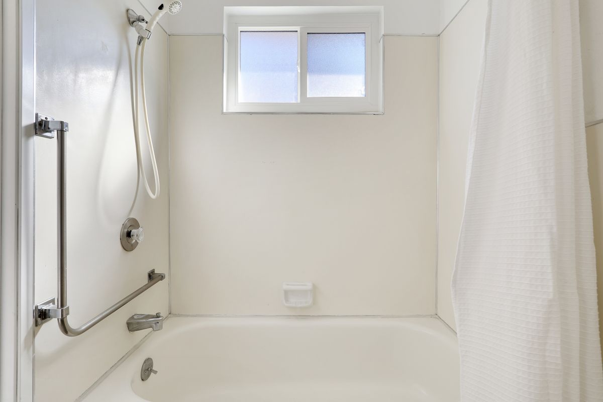 A minimalist bathroom with a bathtub and shower, featuring white walls and a window.