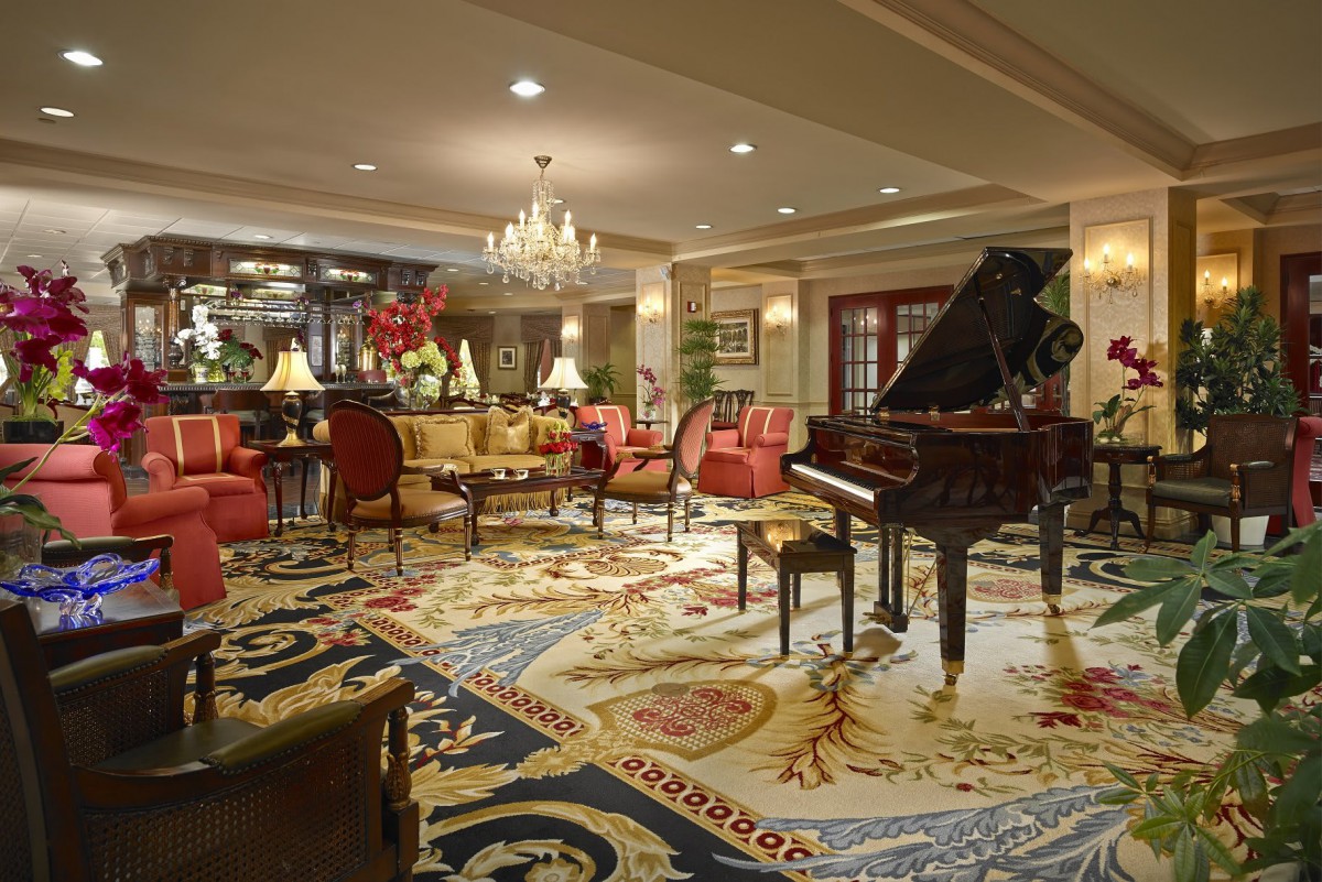 A luxurious hotel lobby featuring a grand piano, elegant seating, and a beautiful chandelier.