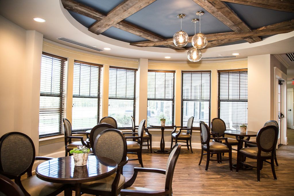 A cozy dining room with round tables, elegant chairs, and large windows letting in natural light.