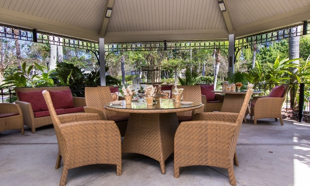 A cozy outdoor seating area under a gazebo with wicker chairs and a well-set table.