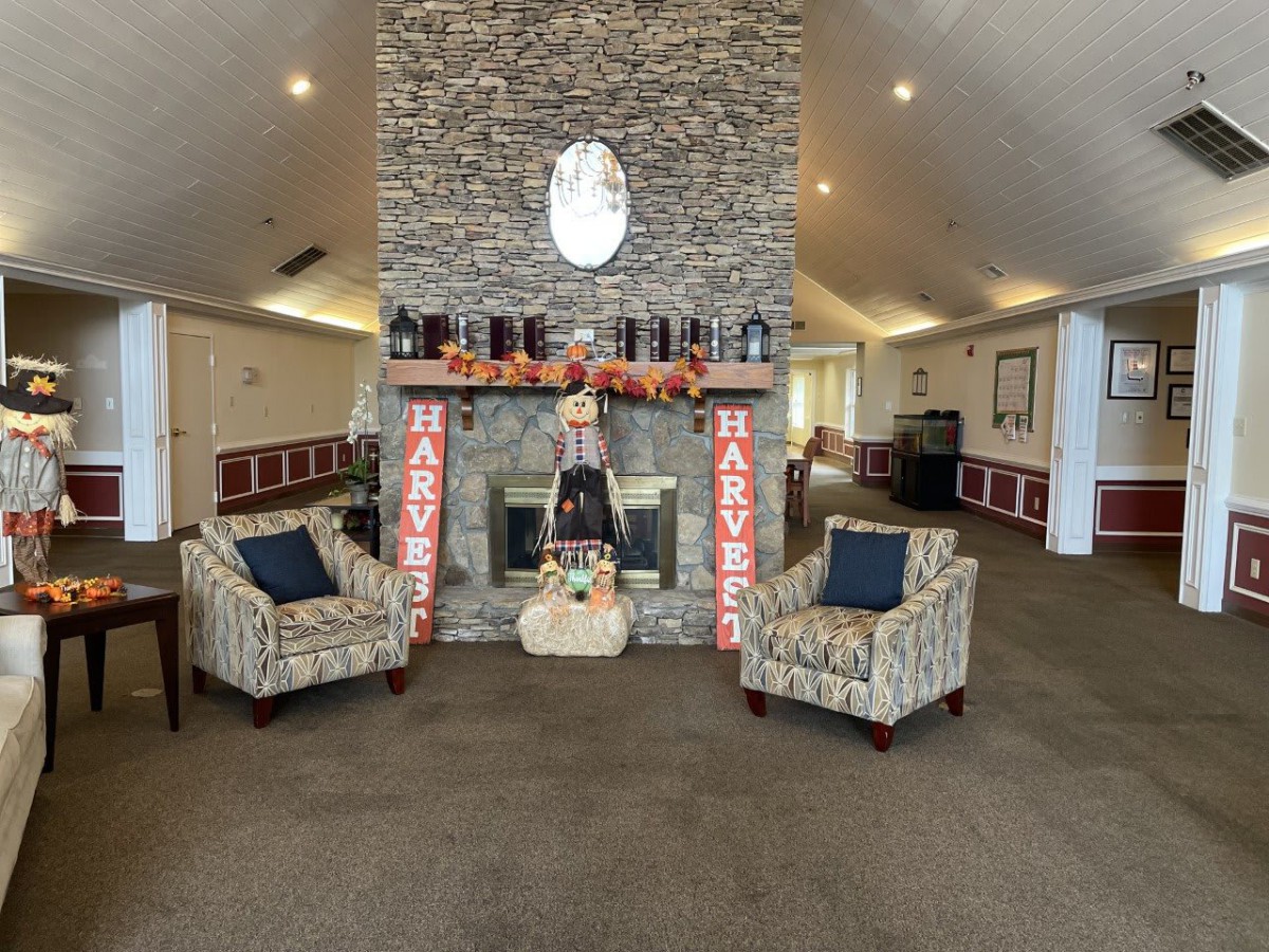 A cozy interior with a decorated stone fireplace featuring autumn decorations and pumpkins, flanked by two patterned armchairs.
