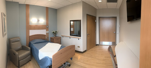 A modern hospital room with a bed, chair, and entrance.