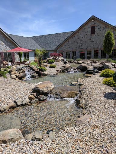 A beautifully landscaped garden featuring a serene water stream, smooth stones, and a picturesque building in the background.