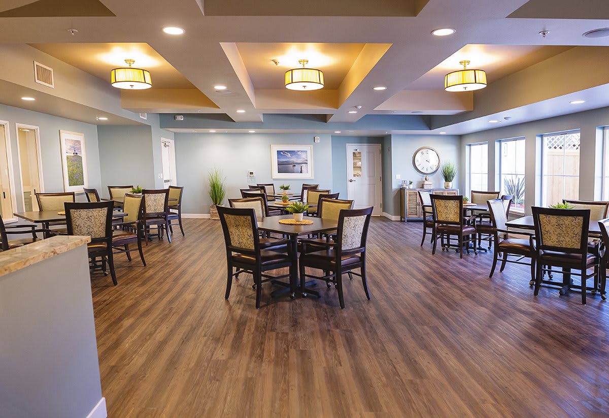 A modern dining area with neatly arranged tables and chairs, featuring warm lighting and a wooden floor.