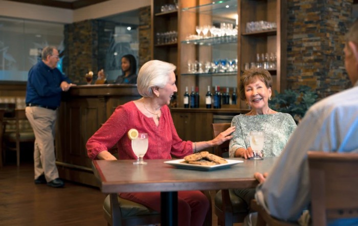 Two elderly women enjoying drinks and laughter at a cafe.