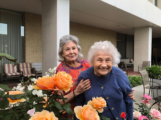 Two elderly women enjoying a sunny day among beautiful flowers.