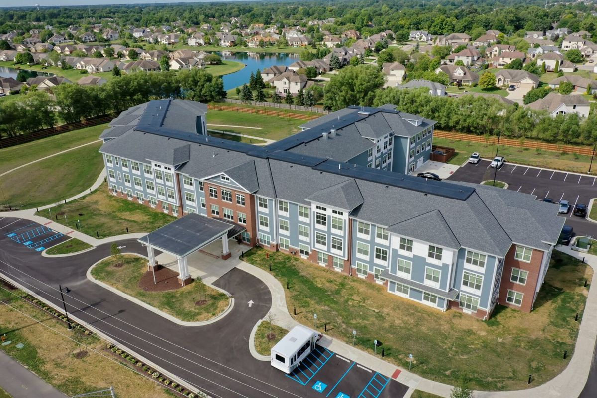 An aerial view of a large residential building surrounded by greenery and neighboring houses.