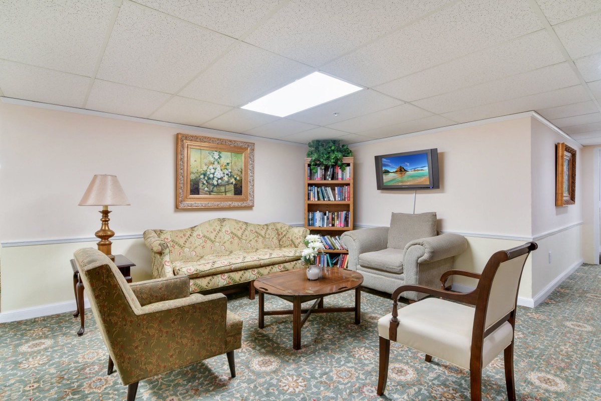 A cozy living room with a sofa, armchairs, and a coffee table, featuring a bookshelf and decorative paintings.
