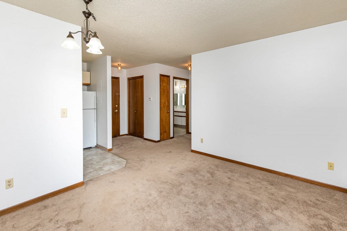 An empty living room with carpeted flooring, white walls, and several doorways.