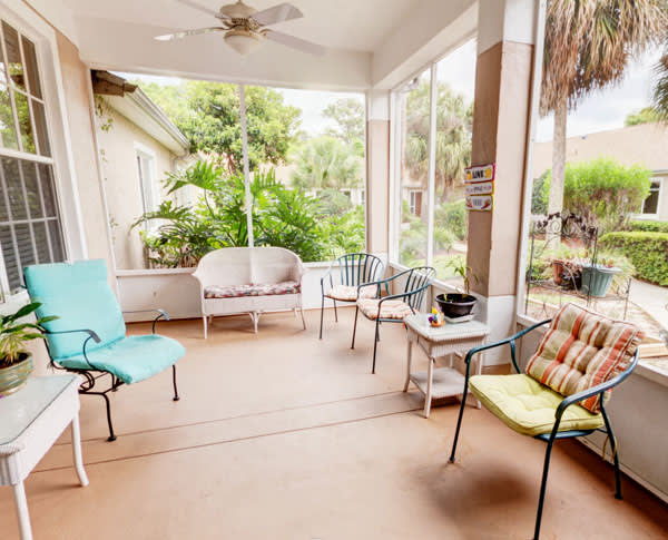 A cozy porch with various chairs and tables, surrounded by lush greenery.