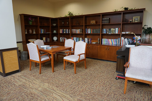 A cozy corner of a library or office featuring wooden bookshelves filled with books, a wooden table, and white upholstered chairs.