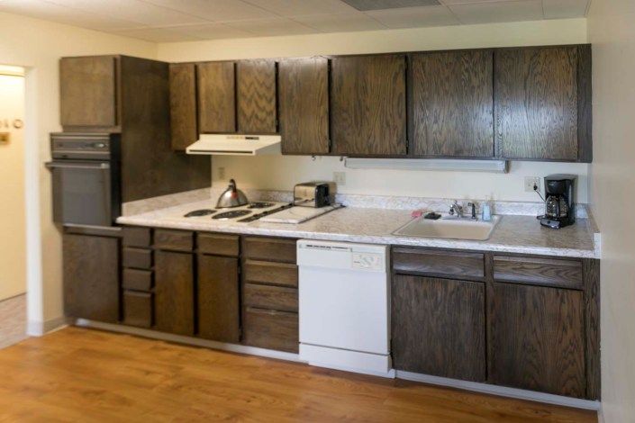 A vintage kitchen with dark wooden cabinets and standard appliances.