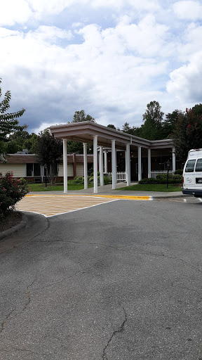 A view of a building entrance with a parking area under a partly cloudy sky.