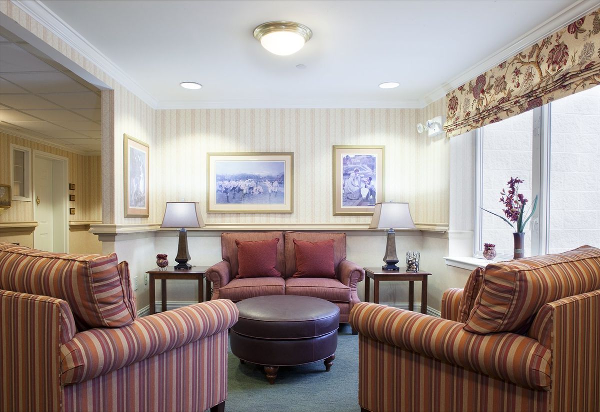 A cozy living room with a sofa and chairs arranged around a coffee table, accented by lamps and artwork on the walls.