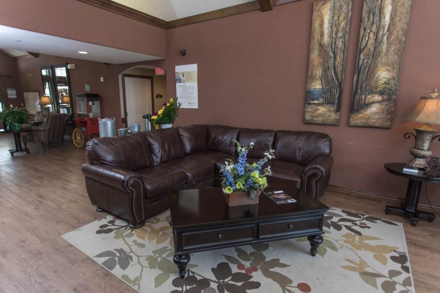A cozy living room with a brown leather sofa and coffee table, complemented by decorative artwork and a patterned carpet.