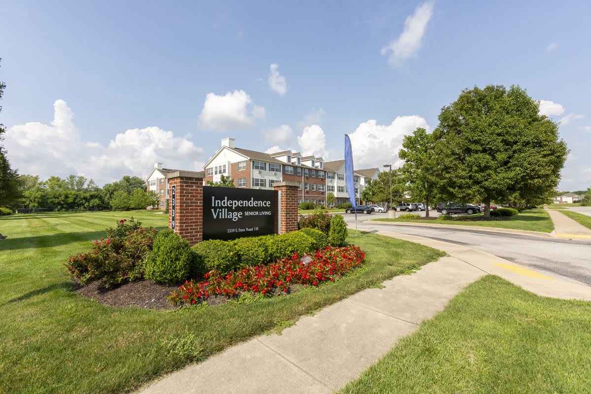 A residential complex entrance with a landscaped garden and sign, under a partly cloudy sky.
