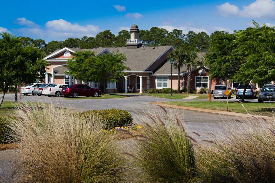 A residential building surrounded by landscaped greenery and parked cars under a clear blue sky.