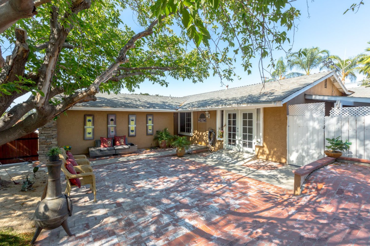 A sunny backyard patio with outdoor seating and a large tree providing shade.