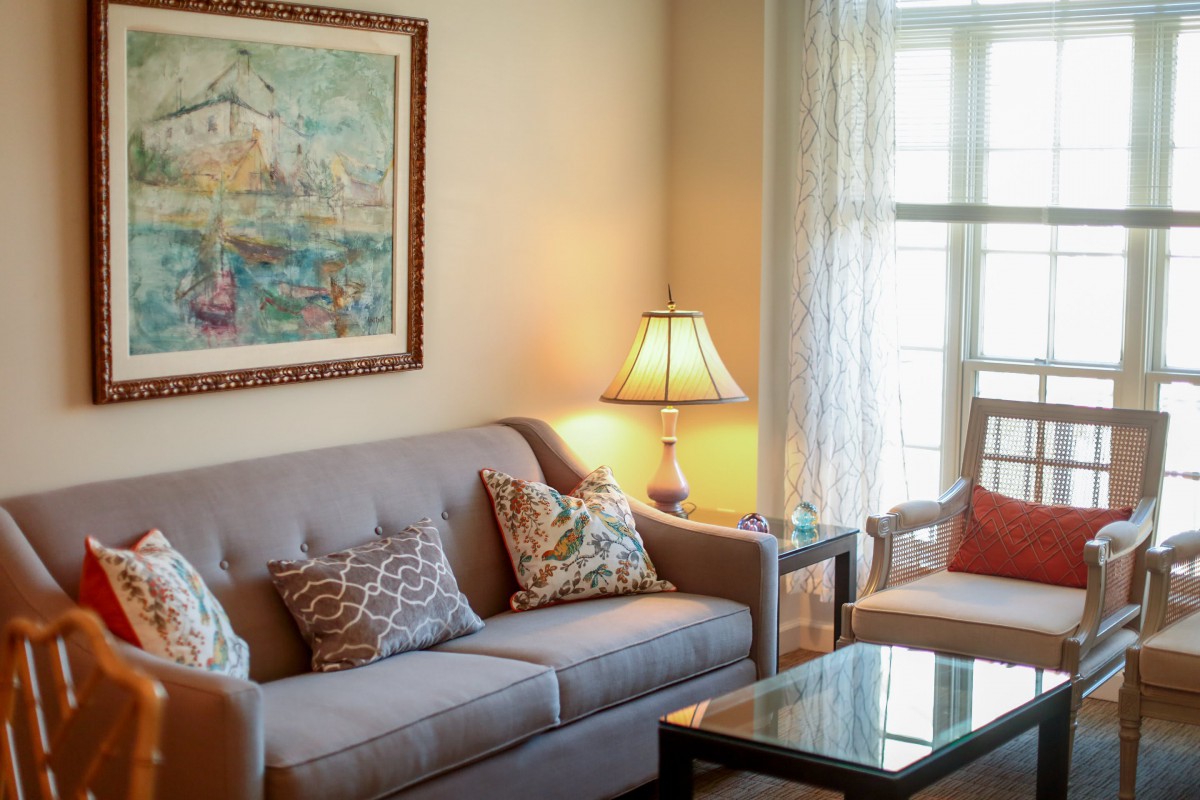 A cozy living room featuring a comfortable sofa with decorative pillows, a lamp, and a painting on the wall.