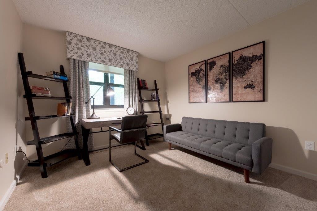 A cozy home office with a desk, chair, and sofa, featuring map-themed wall art.