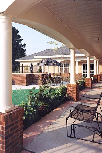 A covered patio area with chairs and columns overlooking a garden.