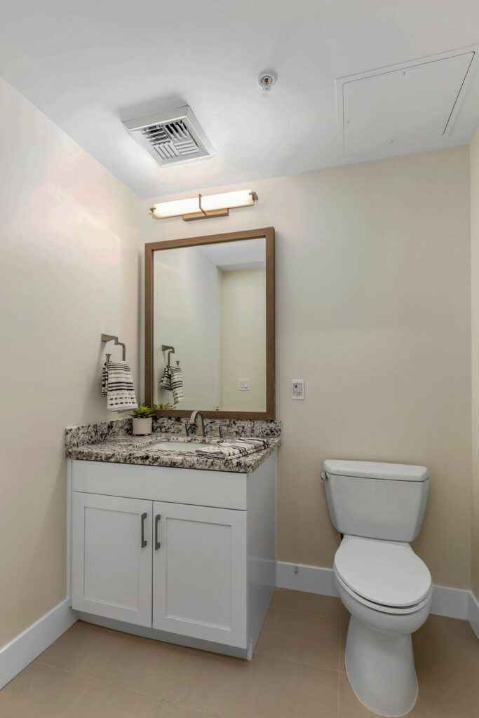 A neatly designed bathroom featuring a vanity with a granite countertop and a wall-mounted mirror above the sink.