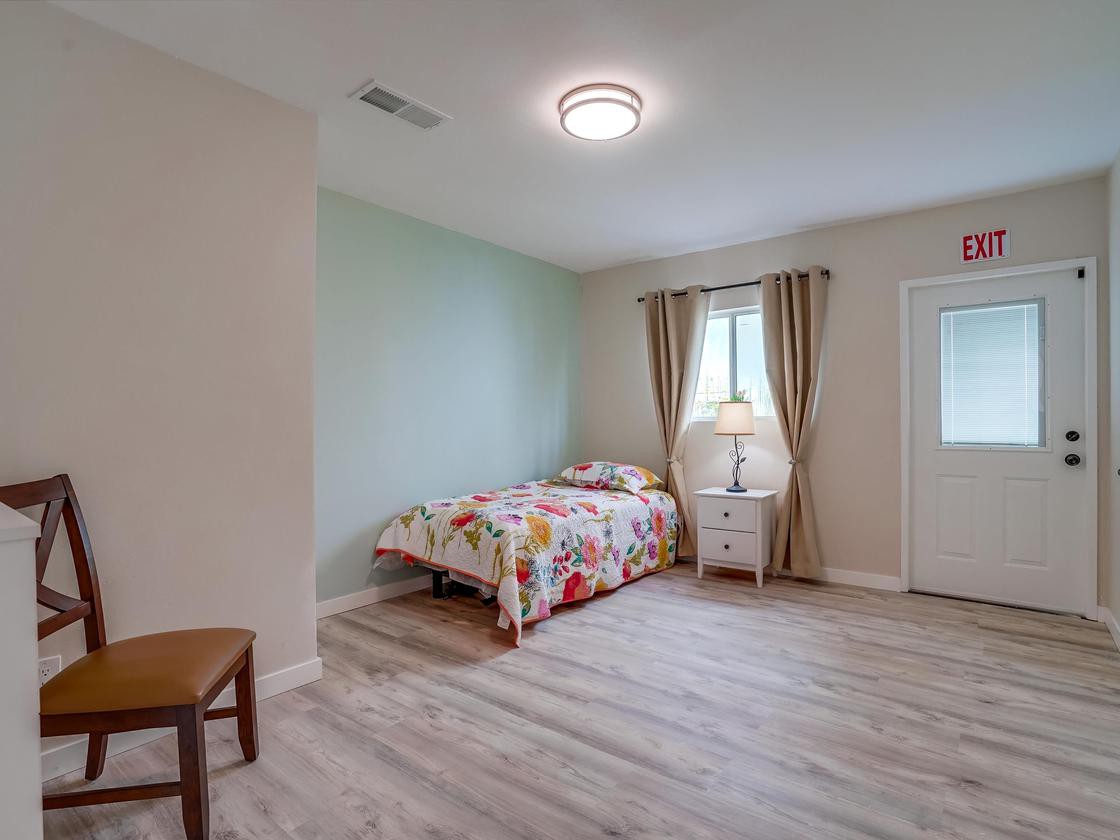 A minimalist bedroom with a single bed, wooden flooring, and a nightstand with a lamp.