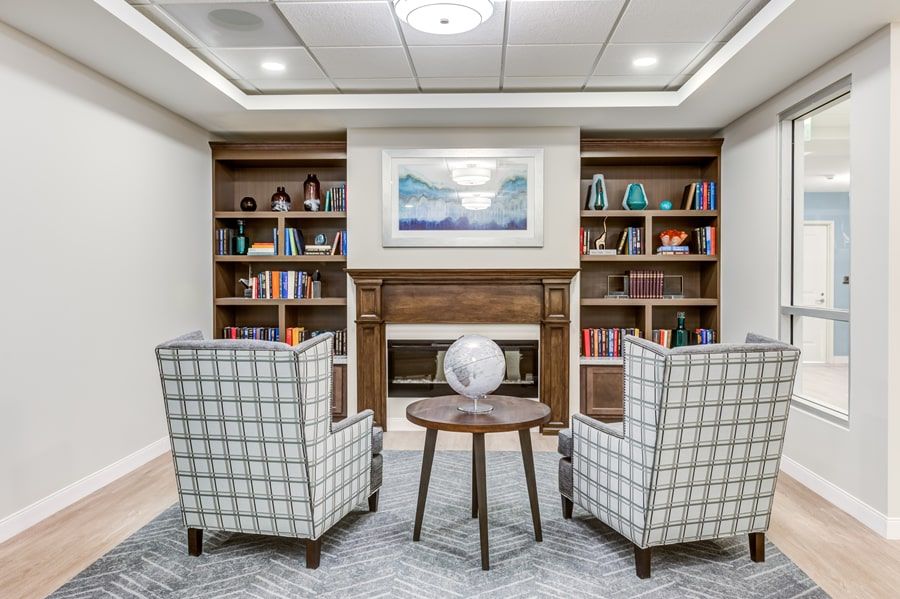 A cozy reading nook with armchairs facing a small table and globe, surrounded by bookshelves filled with various books and decor.